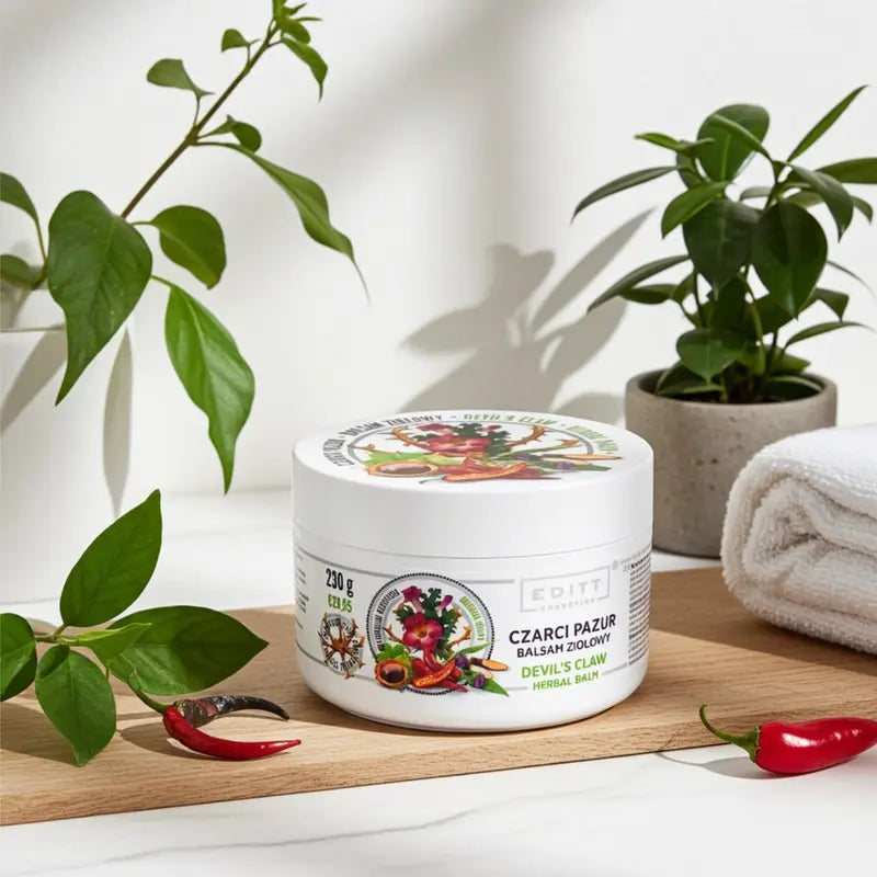 Jar with Devil's claw herbal balm muscle ointment  on a wooden surface with plants and towels in the background